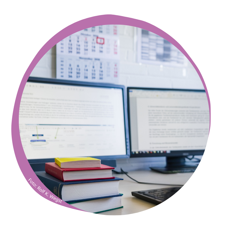 PC-Bildschirme mit Text, davor ein Bücherstapel